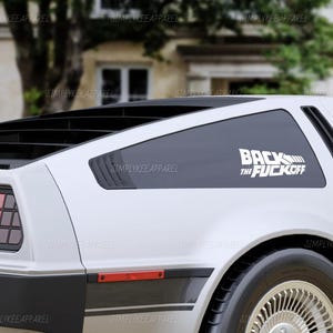 May include: A white car with a black rear window and the text "BACK THE FUCK OFF" in white. The car has a black stripe along the bottom and a red taillight.