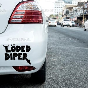 May include: A white car with a black "Loaded Diper" sticker on the back bumper.