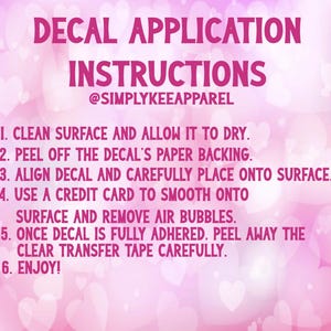 Op de afbeelding: Roze achtergrond met witte harten en instructies voor het aanbrengen van een sticker. De tekst luidt "DECAL APPLICATION INSTRUCTIONS" gevolgd door zes stappen, waaronder het reinigen van het oppervlak en het gladstrijken met een creditcard.