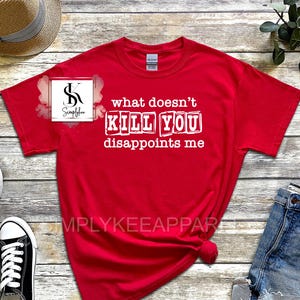 May include: Red t-shirt with white text that reads "what doesn't kill you disappoints me". The text is in a blocky font and appears to be printed on the shirt.