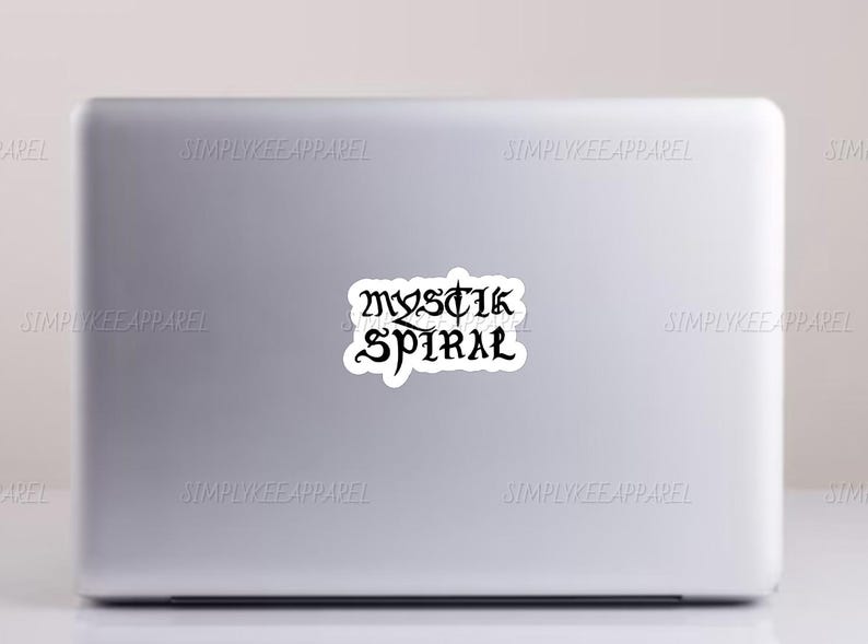 K&ouml;nnte beinhalten: Ein wei&szlig;er Laptop mit einem schwarzen Aufkleber auf dem Deckel, auf dem "MYSTIK SPIRAL" steht.