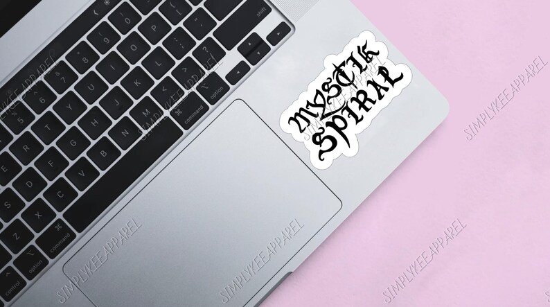 K&ouml;nnte beinhalten: Ein wei&szlig;er Laptop mit einer schwarzen Tastatur und einem schwarz-wei&szlig;en Aufkleber auf dem Trackpad, auf dem "MYSTIK SPIRAL" steht.