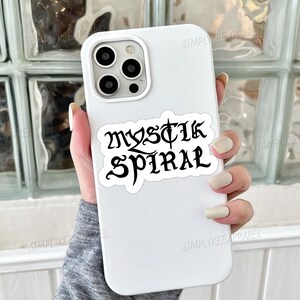 K&ouml;nnte beinhalten: Wei&szlig;es Handy-Case mit einem schwarzen Aufkleber, auf dem in gotischer Schrift "Mystic Spiral" steht.