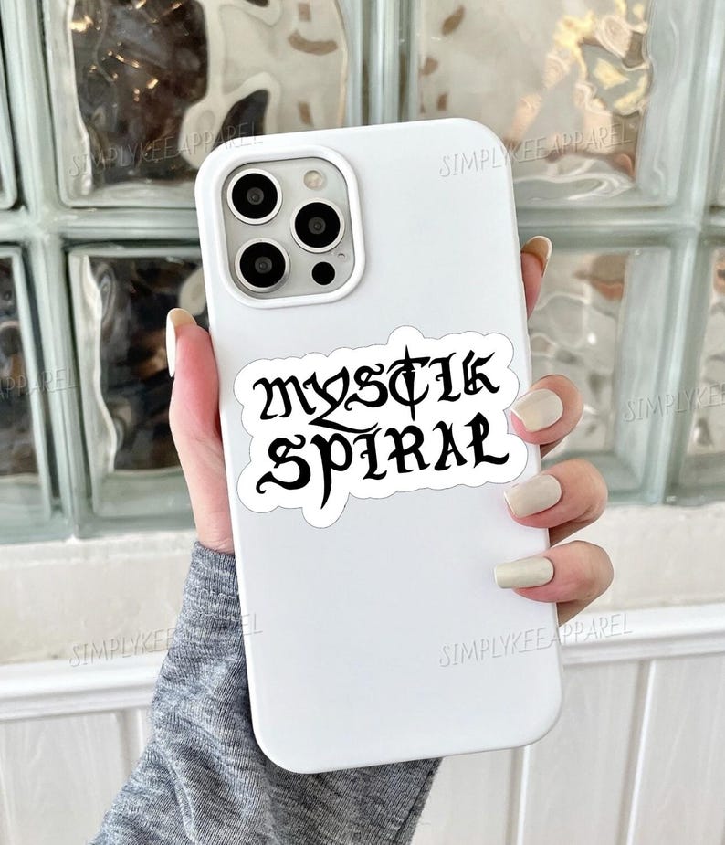 K&ouml;nnte beinhalten: Wei&szlig;es Handy-Case mit einem schwarzen Aufkleber, auf dem in gotischer Schrift "Mystic Spiral" steht.