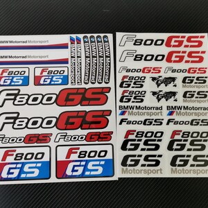 Può includere: Una collezione di adesivi con il marchio BMW Motorrad Motorsport e il testo del modello F800GS. Gli adesivi sono presentati su due fogli bianchi, mostrando varie dimensioni e combinazioni di colori in rosso, blu, nero e bianco.