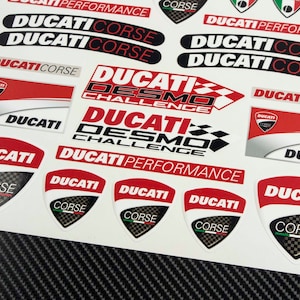 May include: A sheet of red, white, and black Ducati motorcycle stickers. The stickers feature the Ducati logo, the words "Ducati Corse", "Ducati Desmo Challenge", and "Ducati Performance".