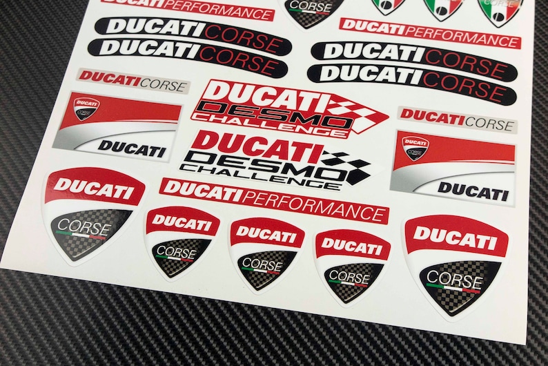 May include: A sheet of red, white, and black Ducati motorcycle stickers. The stickers feature the Ducati logo, the words "Ducati Corse", "Ducati Desmo Challenge", and "Ducati Performance".