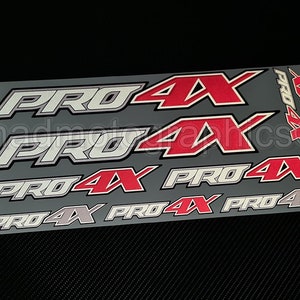 May include: A set of six silver and red decals with the text "PRO 4X" repeated on each decal. The decals are designed for use on a vehicle.