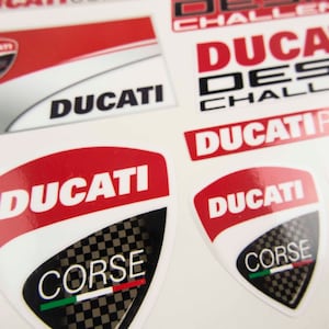 May include: A set of red and white Ducati motorcycle decals with the words "Ducati Corse" and "Ducati Desmo Challenge" in black lettering.