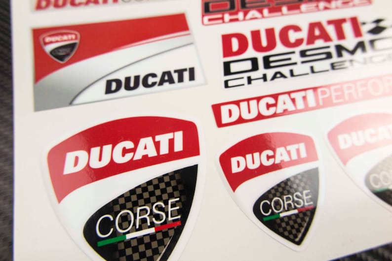 May include: A set of red and white Ducati motorcycle decals with the words "Ducati Corse" and "Ducati Desmo Challenge" in black lettering.