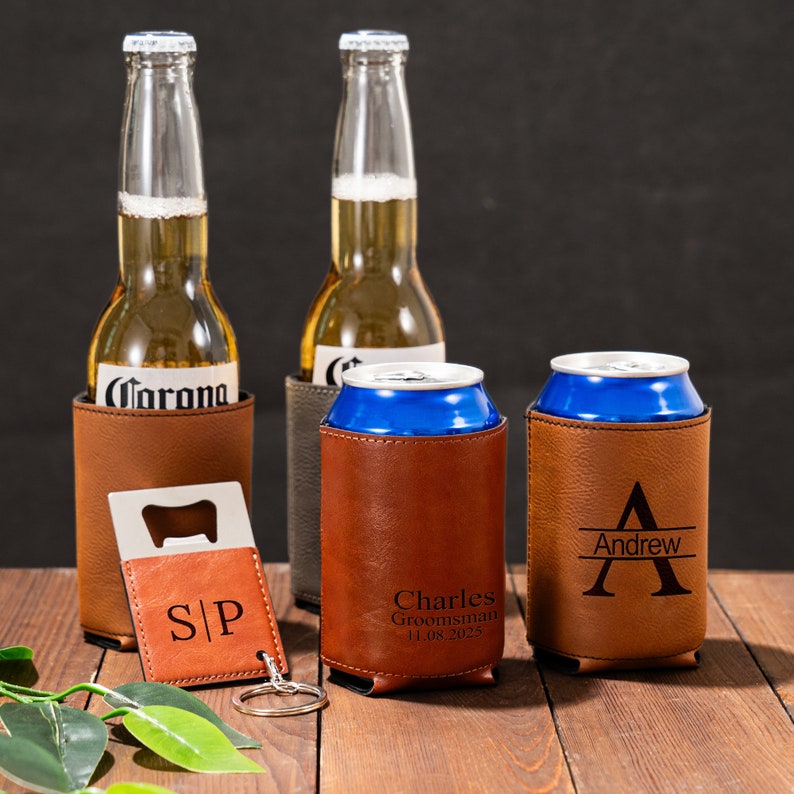 May include: Three brown leather can coolers with personalized names and a bottle opener. The coolers are on a wooden table with a green plant in the foreground.