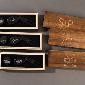 May include: Three wooden boxes with engraved names and golf-themed designs. Each box contains a black golf ball marker and a black golf divot tool.