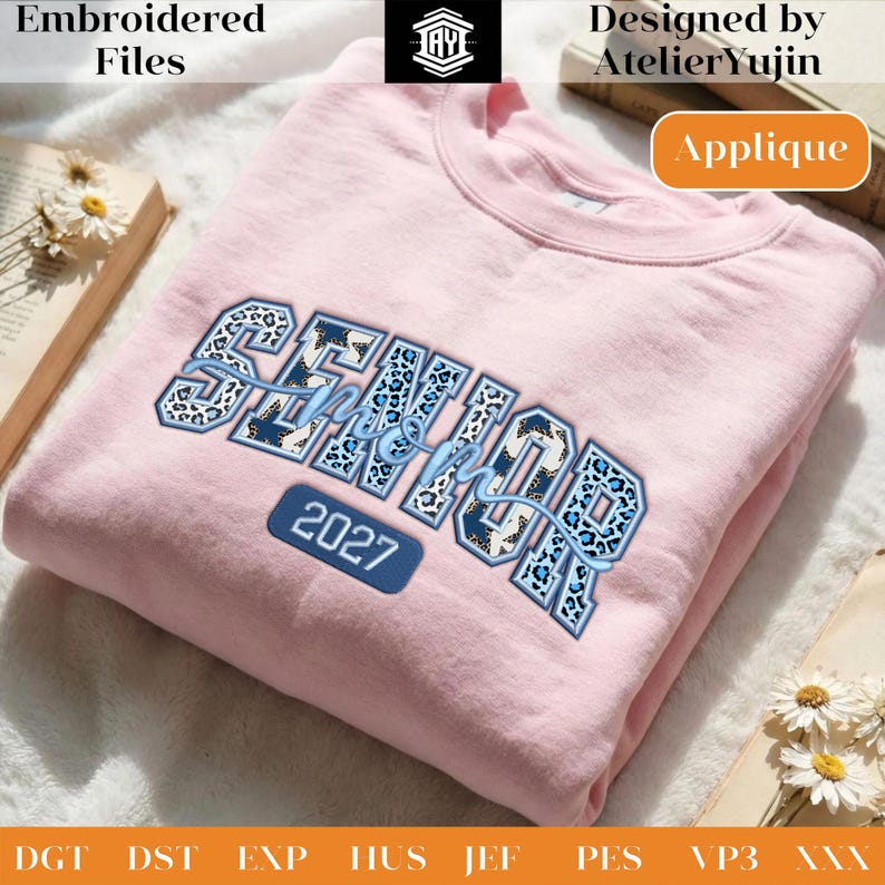 May include: A light pink sweatshirt with the word "SENIOR" in blue and leopard print lettering, and the year "2027" in a blue rectangle. The sweatshirt is embroidered and designed by AtelierYujin.