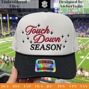 Op de afbeelding: Een wit met zwarte truckerpet met de geborduurde rood en zwarte tekst Touch Down SEASON omringd door kleine sterren. Een holografische sticker op de zwarte klep toont de tekst OTTO CLASSIC OH MY STARS EDITION 002.
