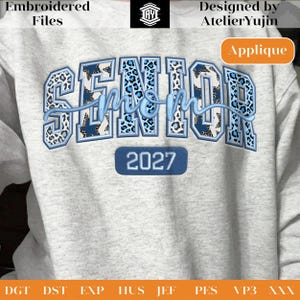 May include: A light gray sweatshirt with the words "SENIOR mom 2027" embroidered in blue and leopard print. The design includes the text "Embroidered Files" and "Designed by AtelierYujin". The word "Applique" is also visible.