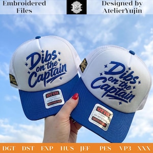 Könnte beinhalten: Zwei weiß-blaue Trucker-Caps mit gesticktem Text Dibs on the Captain und kleinen Sternakzenten. Jede Kappe hat einen blauen Schirm, ein weißes Vorderteil und ein Netzrückenteil. Ein rechteckiger Aufkleber auf dem Schirm zeigt OTTO CLASSIC OH MY STARS EDITION 002.