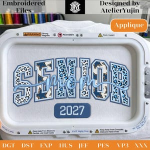 May include: White t-shirt with an embroidered design. The design features the words "SENIOR MOM" in blue and leopard print, with the year "2027" below. The design is set within an embroidery hoop.