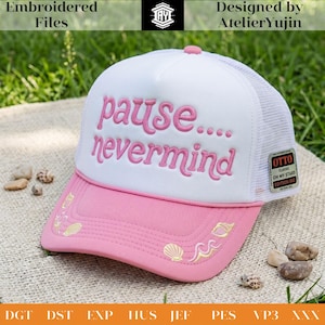 May include: A white and pink trucker hat featuring the embroidered pink text "pause.... nevermind" on the front panel. The brim is pink with gold embroidered seashell and wave accents. A small rectangular tag on the side reads "OTTO CLASSIC".