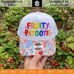 May include: White trucker hat with a floral patterned brim and the embroidered text "FRUITY PATOOTIE" in rainbow colors. The hat features a white mesh back and a curved brim. The hat has a tag that says "OH MY STARS EDITION 002".