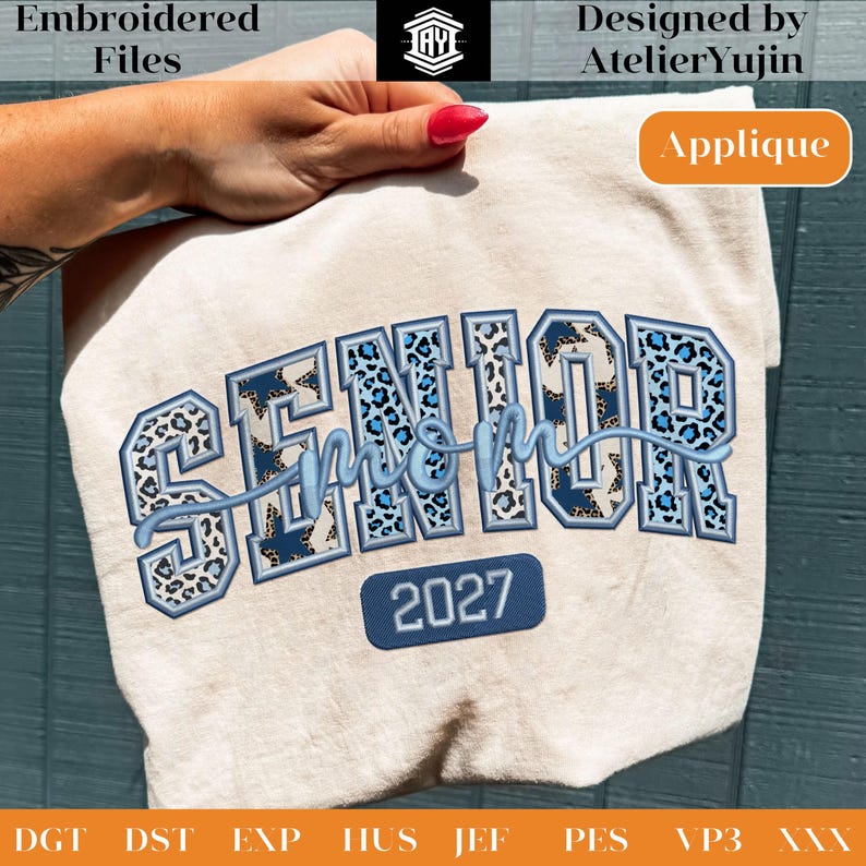 May include: A beige t-shirt with the embroidered text "SENIOR mom 2027". The word "SENIOR" is in a blue leopard print design, and "mom" is in a light blue script. The year "2027" is in a blue rectangle.