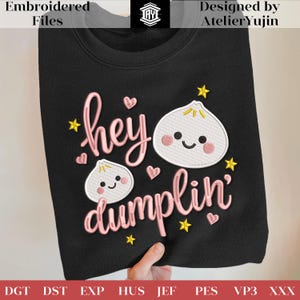 Puede incluir: Sudadera negra con la frase bordada "hey dumplin'" en rosa, con dos ilustraciones de empanadillas con caras sonrientes, corazones y estrellas. El diseño es de AtelierYujin.