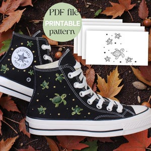 Puede incluir: Zapatillas altas negras con cordones y suelas blancas, adornadas con tortugas marinas verdes bordadas. Las zapatillas presentan el logotipo de Converse All Star y están sobre un fondo de hojas de otoño y bellotas. También se ve un archivo PDF con un patrón imprimible.