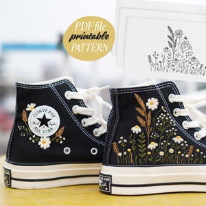 May include: Black high-top sneakers with embroidered floral designs, including daisies and wheat stalks. The sneakers have white laces and soles. A PDF file with a printable pattern is in the background.