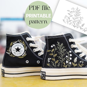 Puede incluir: Zapatillas altas negras con diseños florales bordados y cordones blancos. Una zapatilla presenta el logo de Converse All Star, la otra un patrón botánico. También se ve un archivo PDF con un patrón imprimible.