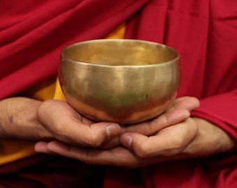 May include: A person holding a golden singing bowl in their hands. The bowl is smooth and shiny, and the person's hands are cupped around it.