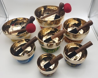 May include: A set of eight singing bowls with wooden strikers and colorful cushions. The bowls are made of brass and have a hammered finish.