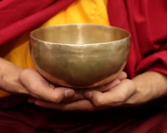 May include: A person wearing a red and yellow robe holds a large, golden singing bowl in their hands.