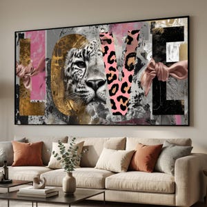 May include: A framed wall art print with the word "LOVE" in a collage style. The "L" is gold, the "O" features a leopard's face, the "V" is pink with leopard print, and the "E" is black and white. Pink ribbons accent the sides.