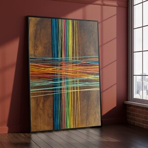 Op de afbeelding: Een ingelijst abstract kunstwerk met een houten paneel en kleurrijke touwtjes. Verticale touwtjes in blauw, groen, geel en oranje kruisen horizontale touwtjes, waardoor een levendig, geometrisch ontwerp ontstaat. Het kunstwerk wordt tentoongesteld tegen een rode muur.