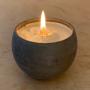Könnte beinhalten: Ein schwarzer Kerzenhalter aus Keramik mit einer weißen Kerze darin. Die Kerze ist angezündet und die Flamme ist sichtbar.