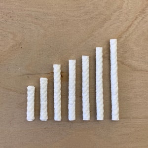 Könnte beinhalten: Sieben weiße Kerzen-Dochte in verschiedenen Längen, in einer Reihe vom kürzesten zum längsten auf einer hellbraunen Holzoberfläche angeordnet.