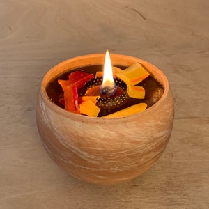 Könnte beinhalten: Ein Terrakotta-Kerzenhalter mit Marmorierung, gefüllt mit geschmolzenem Wachs und bunten Wachsstücken. Eine Flamme brennt von einem Docht in der Mitte des Halters.