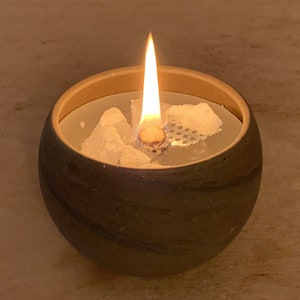 Könnte beinhalten: Ein brauner Kerzenhalter aus Keramik mit einer weißen Wachskerze darin. Die Kerze ist angezündet und die Flamme ist sichtbar.