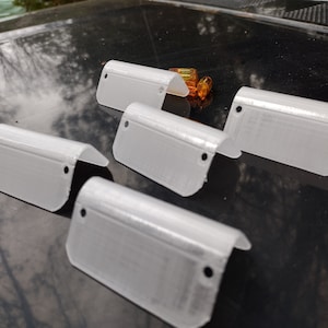 May include: Six white plastic corner guards with rounded edges and a hole in the center. The guards are arranged in a semi-circle on a black surface.