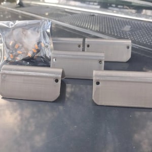 May include: Five gray plastic parts with rounded edges and two small holes on each side. The parts are arranged in a row on a gray surface.
