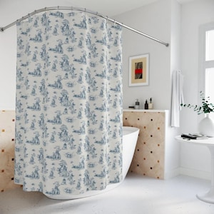 Pode incluir: Um cortina de chuveiro branco com um padrão de toile azul e branco que apresenta um desenho repetitivo de árvores e casas. A cortina de chuveiro está pendurada em um banheiro com uma banheira branca e uma parede de azulejos brancos.