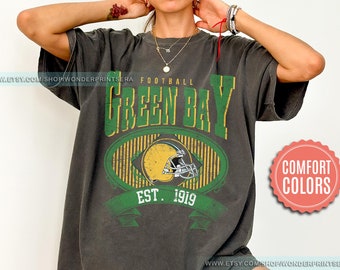 May include: A dark gray t-shirt with a vintage-style graphic of the Green Bay Packers logo. The logo features a green and yellow football helmet with the text "Football Green Bay Est. 1919".