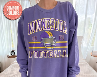 May include: Purple sweatshirt with a vintage-style graphic of a football helmet and the text "MINNESOTA FOOTBALL 19 61".