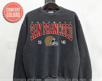 May include: A dark gray sweatshirt with the text "FOOTBALL SAN FRANCISCO 19 46" in red and white lettering. A brown and red football helmet graphic is centered below the text.
