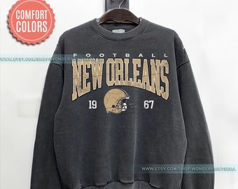 May include: A black sweatshirt with a vintage-style graphic of the New Orleans Saints football team. The graphic features the team's name in gold lettering, a football helmet, and the years 1967 and 19.