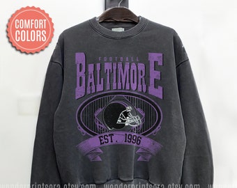 May include: A black sweatshirt with a purple distressed graphic of a football helmet and the text "FOOTBALL BALTIMORE EST. 1996".
