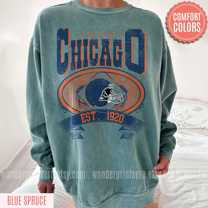 May include: A teal blue sweatshirt with a vintage-style graphic of a football helmet and the text "FOOTBALL CHICAGO EST. 1920".