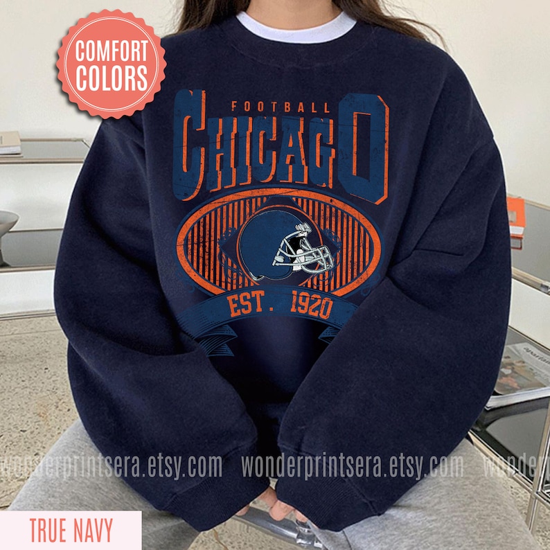 May include: A navy blue sweatshirt with a vintage-style graphic of the Chicago Bears logo. The graphic features the team's helmet, the words "Football Chicago" and "Est. 1920".