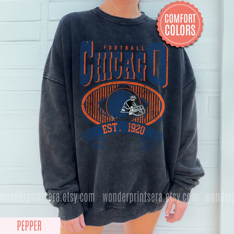 May include: A black sweatshirt with a vintage-style graphic design featuring the text "Football Chicago Est. 1920" and a football helmet in blue and orange.