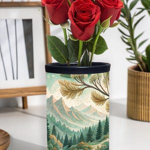 Könnte beinhalten: Eine zylindrische Vase mit dunkelblauem Rand und Landschaftsdesign, die mehrere leuchtend rote Rosen enthält. Die Vase zeigt eine Berg- und Waldszene in Grün-, Blau- und Beigetönen. Die Rosen haben grüne Blätter.