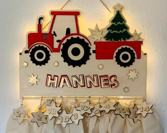 May include: A wooden advent calendar shaped like a red tractor pulling a wagon with a Christmas tree. The calendar has 24 numbered pouches for gifts. The name "HANNES" is written on the top of the calendar.